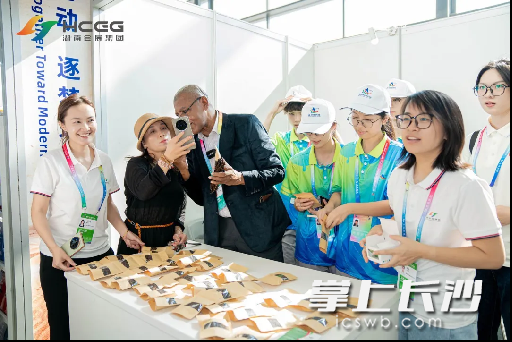 展位前，志愿者纷纷帮助科Chahalane介绍展品。