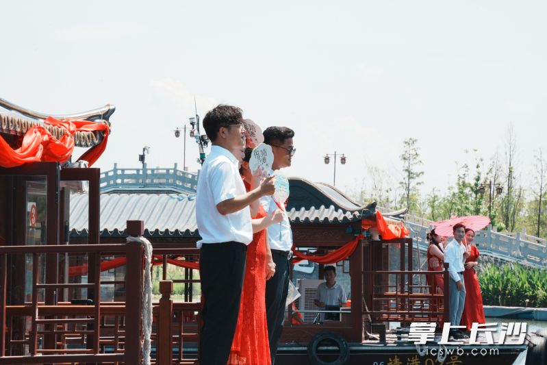 新人们身着传统婚服站在船头，笑容与粼粼波光相映成趣。