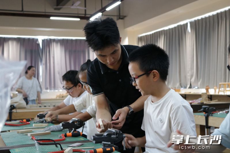 孩子们在老师的指导下制作木制坦克、飞机等国防主题作品。