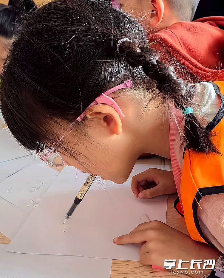 在“含笔书写”环节，孩子们尝试用嘴巴咬住笔杆书写简单文字。