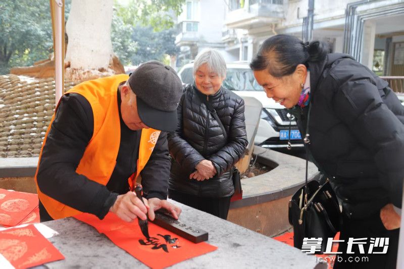 书法爱好者们挥毫泼墨，承载着祝福的春联被送到居民手中。