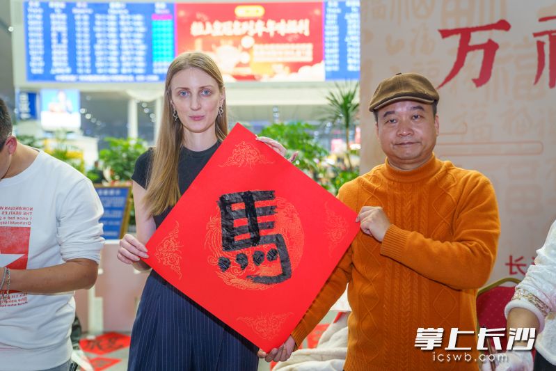 俄罗斯姑娘萨沙连续三年在长沙南站新春送“福”。今年，她携书法新作再度亮相，成为人群中的亮眼风景。 均为长沙晚报全媒体记者邓迪摄