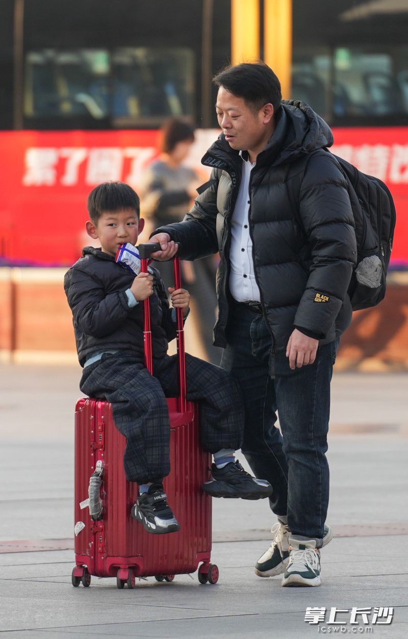 一个小孩坐在万向轮的行李箱上前行。