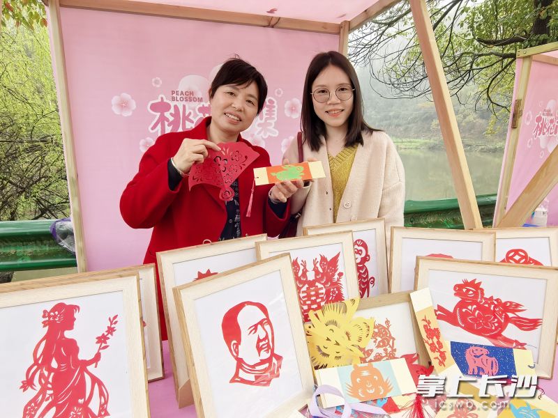 灰汤本土剪纸艺人张静（左）现场展示精湛手艺，并将剪纸作品赠送给游客。