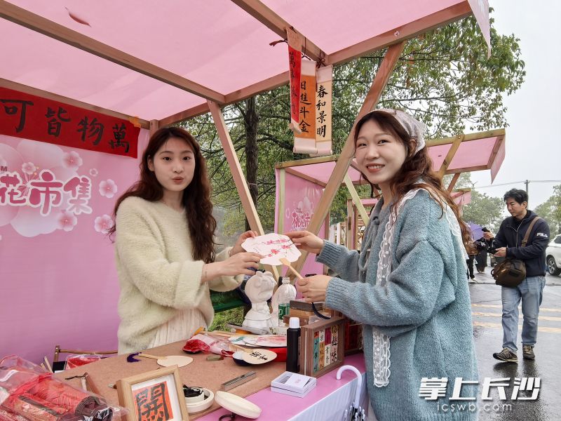 桃花手工DIY区，谢映华、谢映红姊妹花默契打理着摊位，并指导游客制作桃花书签、饰品等。