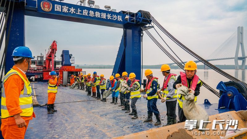 抢险队员以人链传递沙袋，经装载机转运至堤顶，实现 “水上制袋、岸边接驳、堤顶筑堤”高效作业。