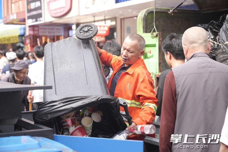 在人来人往的黄兴路步行街，环卫工人搬运着大型垃圾桶，守护城市环境卫生。