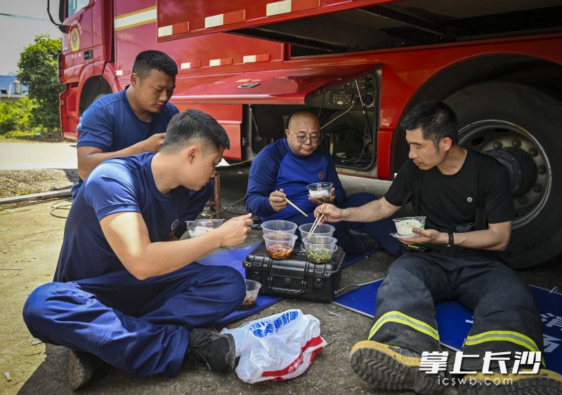救援间隙，消防队员在烈日下抓紧吃工作餐。
