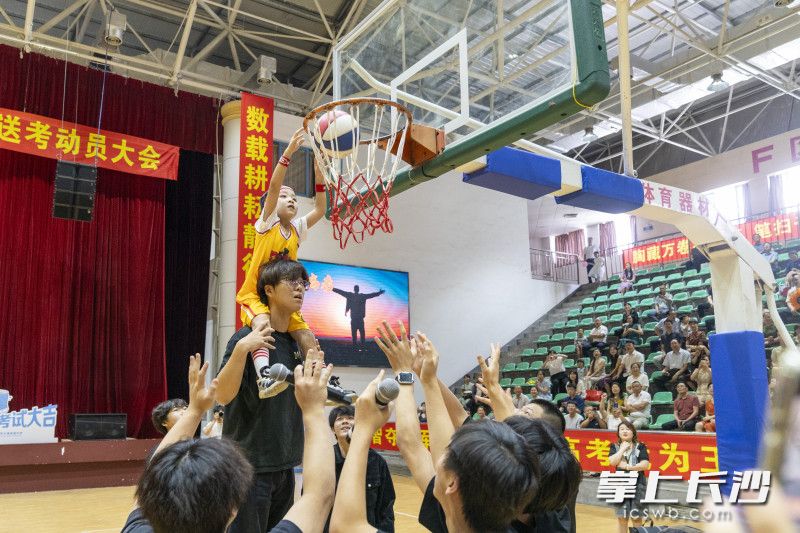“投篮助考”：几位身高突出的高中男生将幼儿园大班小朋友扛在肩上，由小朋友将篮球投入篮筐，寓意“高考必中”。