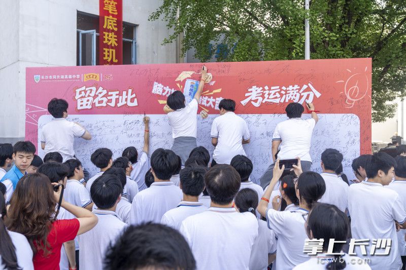 高考前一天，长沙市同升湖高级中学校园内竖立巨型签名展板，高三考生轮番腾空摸高、落笔签名。