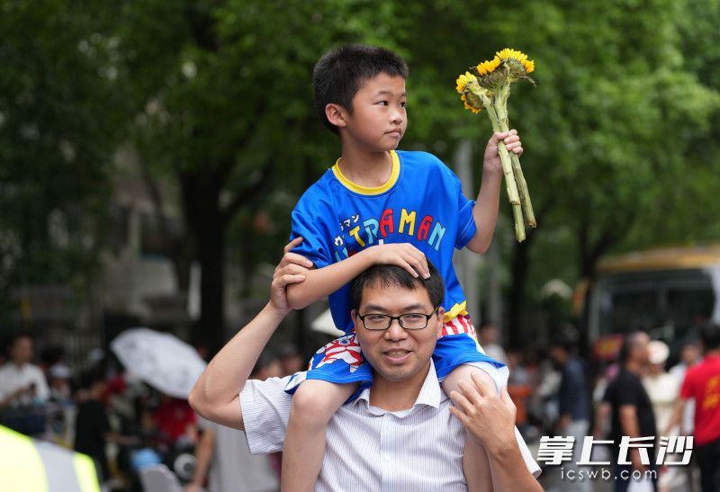 6月7日，湖南师范大学附属中学考点，一位家长带着手持向日葵的弟弟来给考场内的哥哥姐姐加油鼓劲。均为长沙晚报全媒体记者 邹麟 摄