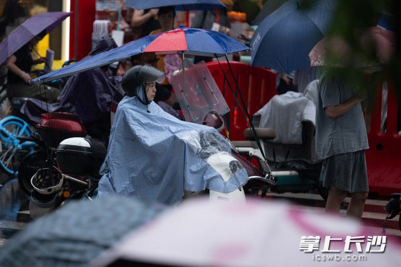 大雨中，家长骑车电动车穿着雨衣等候下考的孩子。