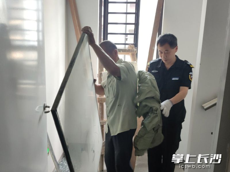 物业工作人员帮助居民清理楼道堆物，畅通“生命通道”。