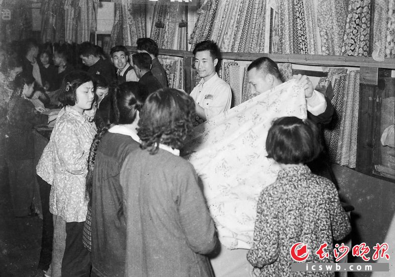 1954年4月25日，公私合营后的八角亭江浙绸布店，增加经营品种，设立了花布专柜，陈设了150多种新艳花布。图为营业员热忱服务，帮顾客挑选衣料。