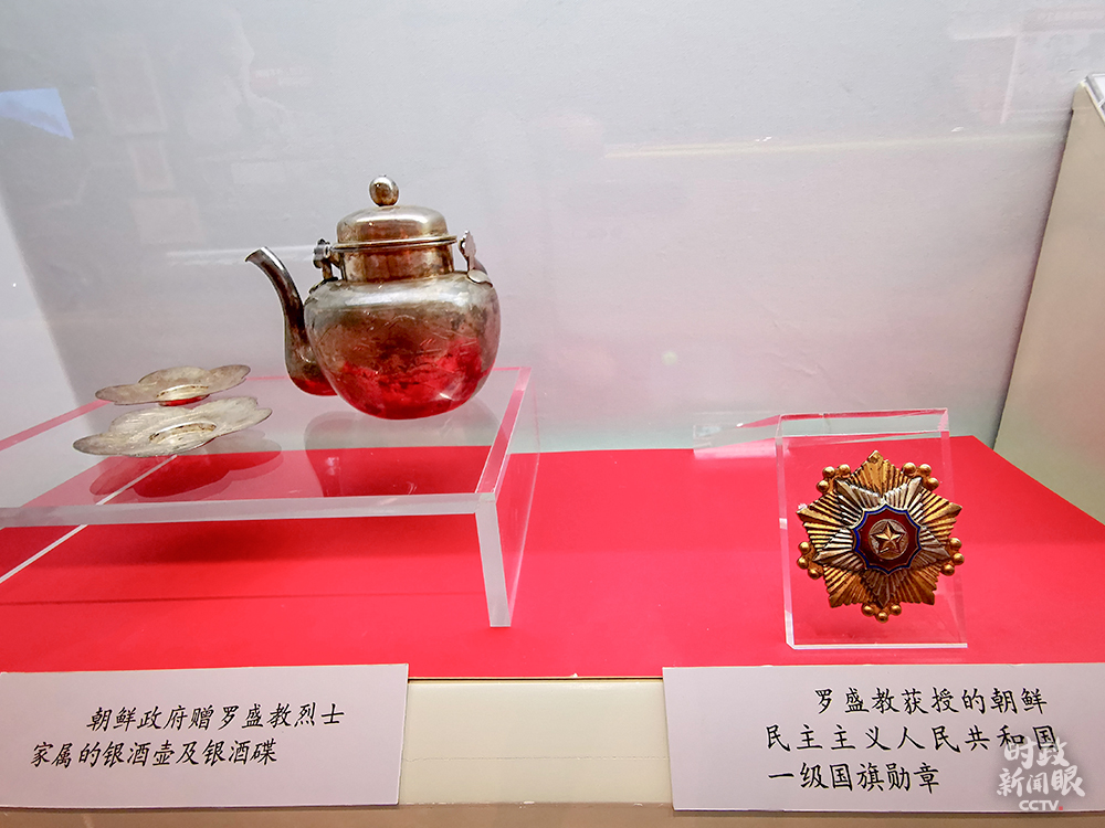 △左为朝鲜政府赠给罗盛教烈士家属的银酒壶、银酒碟，右为罗盛教获授的朝鲜民主主义人民共和国一级国旗勋章。（总台央视记者荆伟拍摄）