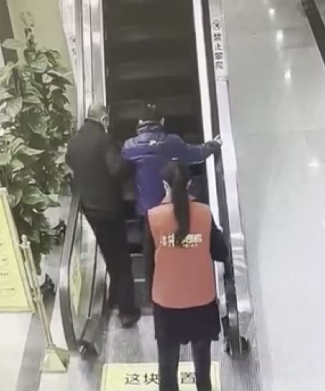 志愿者丰云不放心，站在老人身后守着，看着他上扶梯。 视频截图