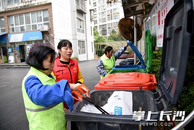 麓谷街道锦绣社区麓山润城小区志愿者在桶边检查垃圾是否投放准确。