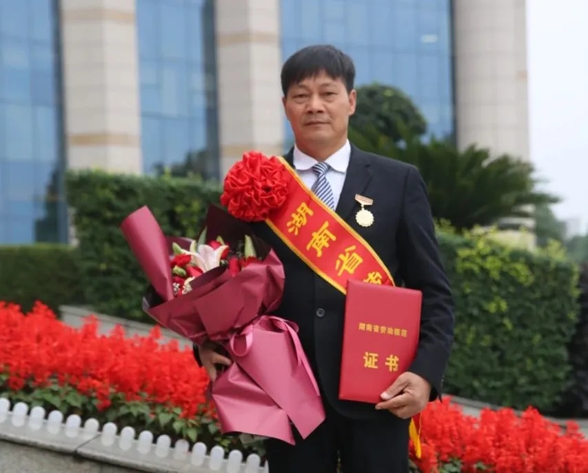 ▲周科明手拿“湖南省劳动模范”证书，佩戴劳模徽章照片。