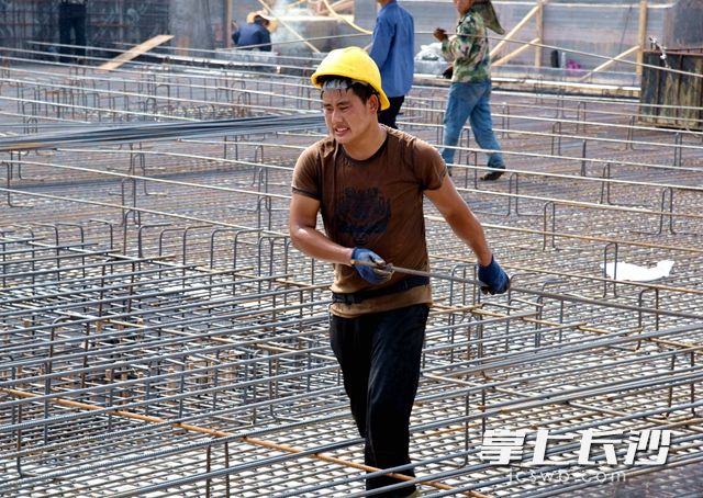  建筑工人杨世标带着手套，正在奋力搬运着钢筋。