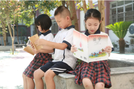 ▲学生在校园树荫下诵读，享受欢乐时光。