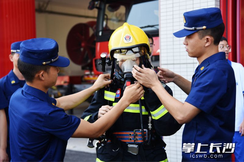 在消防员的帮助下，一名学生体验穿灭火战斗服，佩戴空气呼吸器。