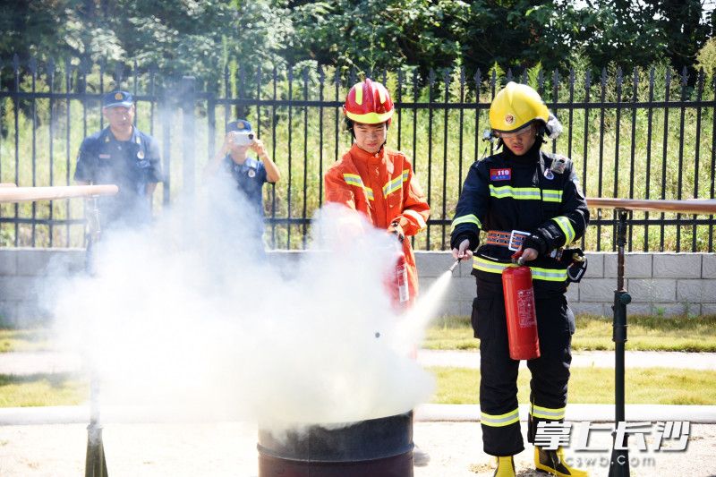 两名身穿消防服装的学生学习用灭火器灭火。