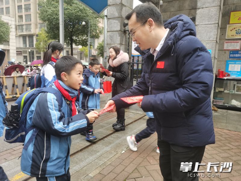 2月11日是开福区清水塘第三小学开学报到的日子，为迎接返校学生，校长谢益林一大早来到校门口一边向学生送上新年祝福，一边给他们派发开学“红包”。均为长沙晚报全媒体记者 舒文 摄