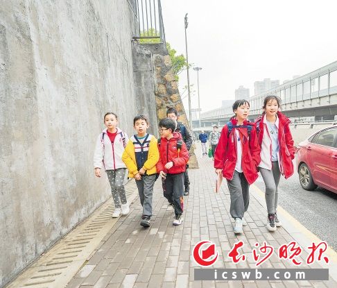 紧靠着护坡，一条窄窄的人行道已经铺设完毕，标识清晰，路面平整略高于一侧车道，孩子们正从容走过。 长沙晚报全媒体记者 陈飞 摄