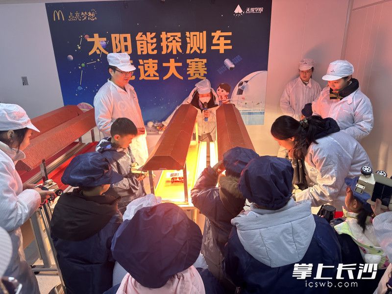 孩子们将自己制作的太阳能探测车放在太阳能灯下比速度。