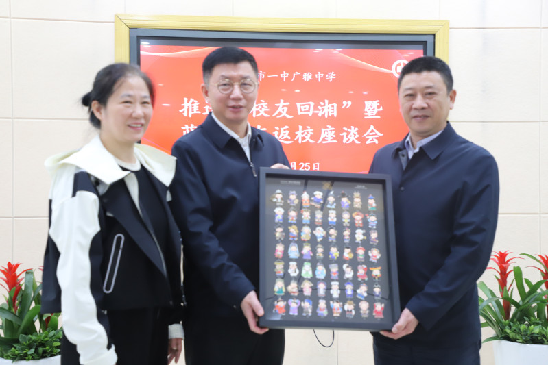 蓝军（中）给学校赠送了一套56个民族娃娃卡通形象徽章作为礼物。长沙市一中广雅中学校长吴军（右）和党委书记戴萍（左）接收礼物。