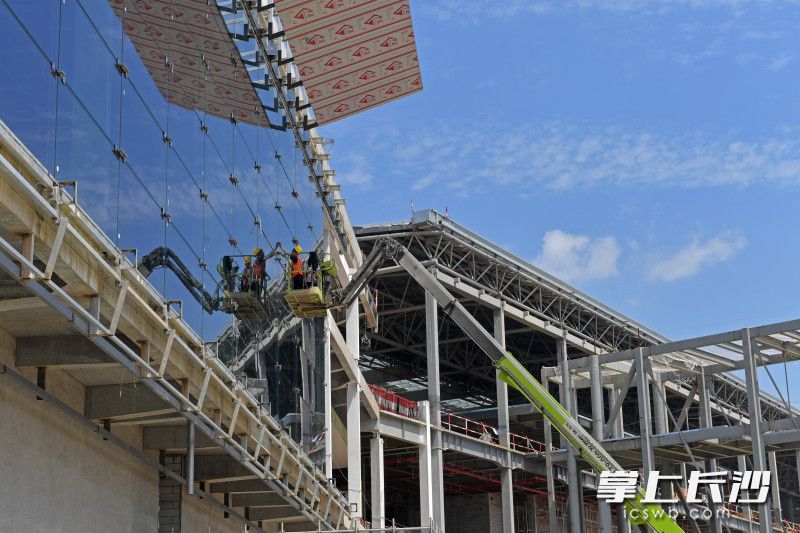 高空作业平台车上，来自怀化的张仁军、张荣健父子俩顶着烈日给玻璃幕墙上的超大玻璃打胶。